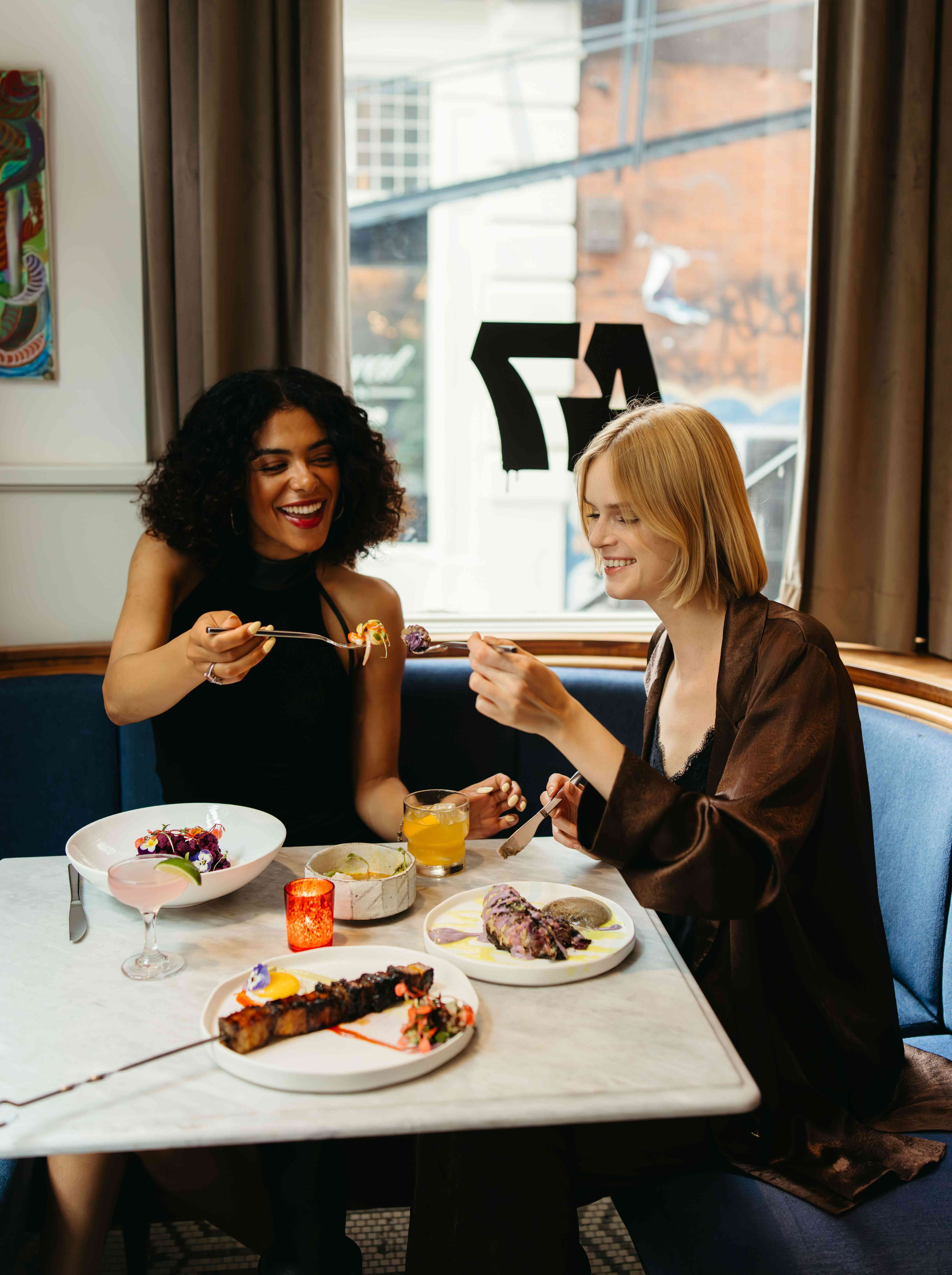 Two women sitting in a booth at a table with food and drinks.