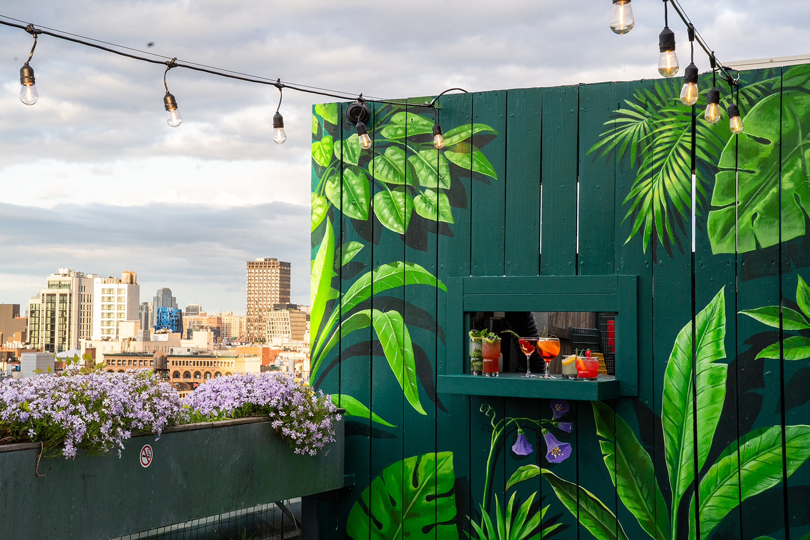 A rooftop bar with a mural, string lights, and a city view.